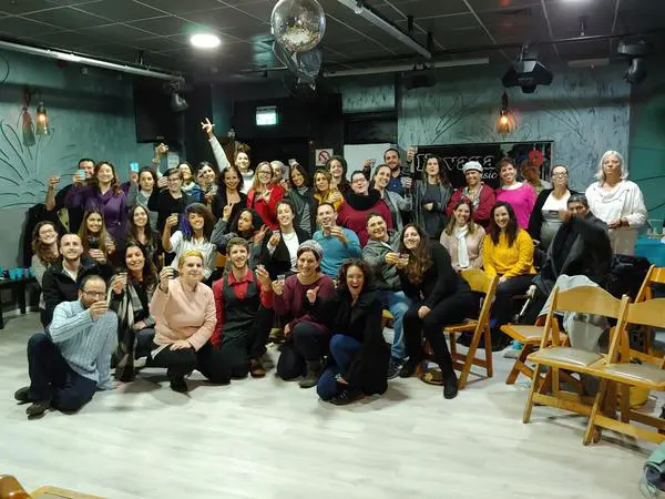 קבוצה של אנשים מקובצים יחד בחדר הרצאות בשלוש שורות, חלק עומדים וחלק יושבים, מרימים כוסית.